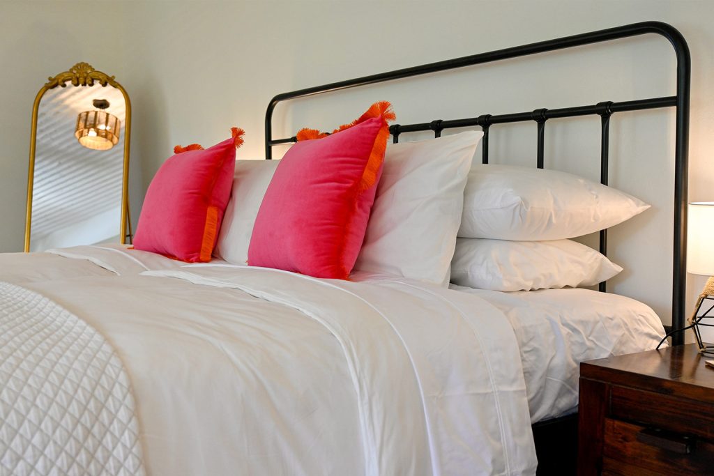 “Cozy master bedroom at Hacienda Eterna Primavera, with soft white bedding and a bright pink pillow, offering a luxurious and relaxing escape in Puerto Rico.”