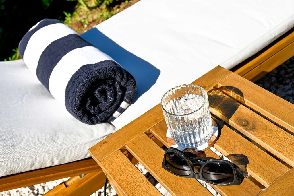 “Outdoor lounge chair at Hacienda Eterna Primavera with a glass of cold water and sunglasses, inviting guests to relax in the tropical garden setting.”