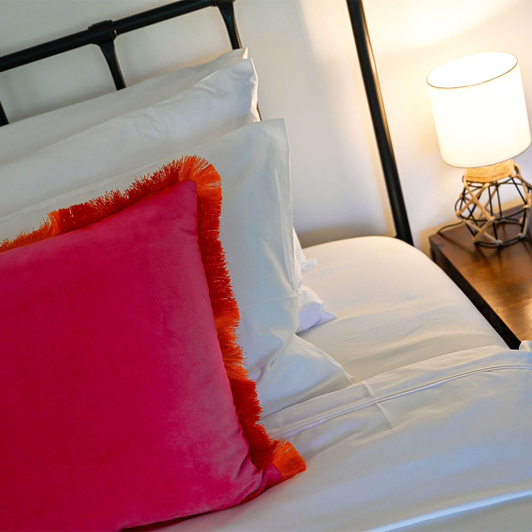 Luxury master bedroom with crisp white bedding, a vibrant red accent pillow, and soft ambient lighting.