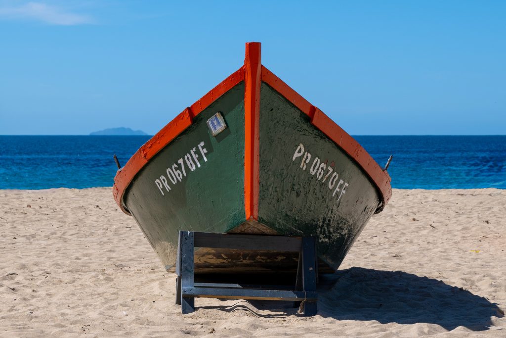 Traditional fishing boat painted green and red, resting on the sandy shore of Puerto Rico with a calm blue ocean in the background.