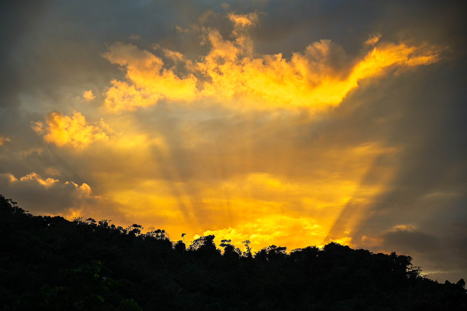 Golden sunset light beams break through clouds over tropical hills in Puerto Rico, seen from the master suite.