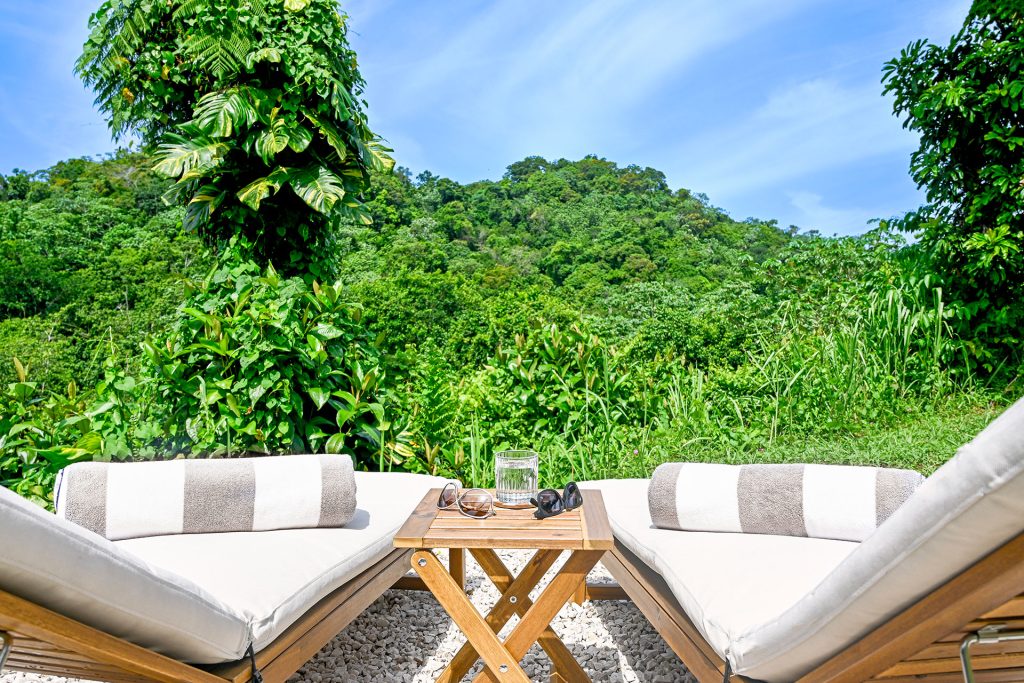 Outdoor lounge area with a wooden table, sun loungers, and a lush green mountain backdrop — perfect for soaking in the tropical tranquility at Hacienda Eterna Primavera.