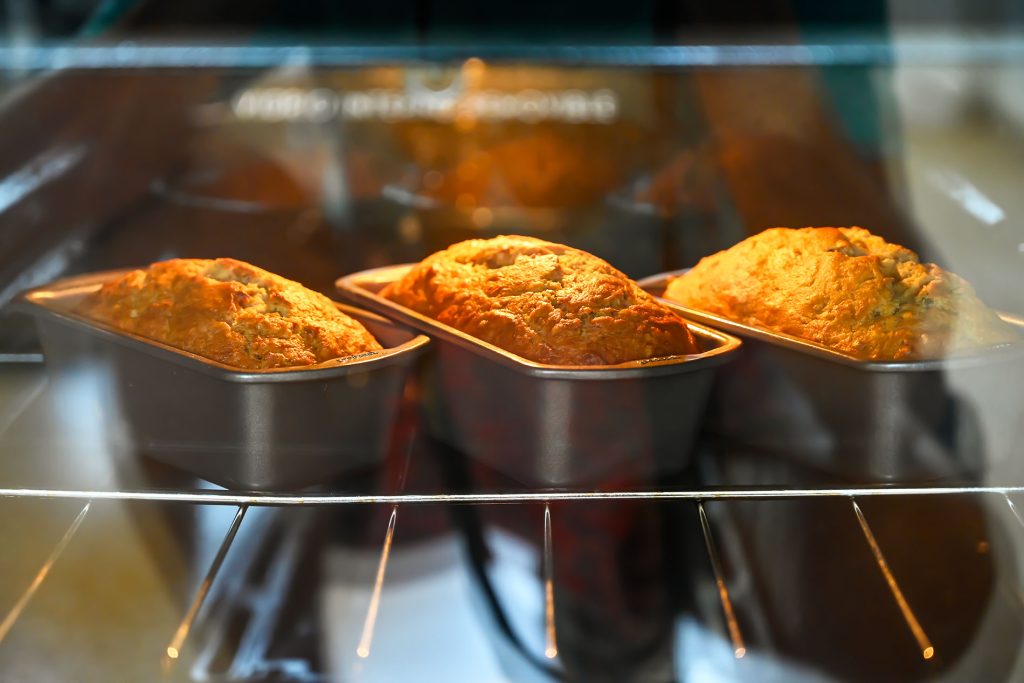 Fresh banana bread loaves baking in the oven at Hacienda Eterna Primavera, showing their golden crust rising during the process.
