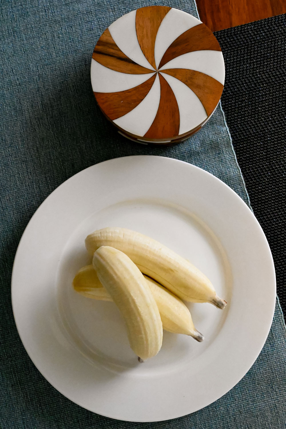 Small bananas arranged on a white breakfast plate on a blue placemat