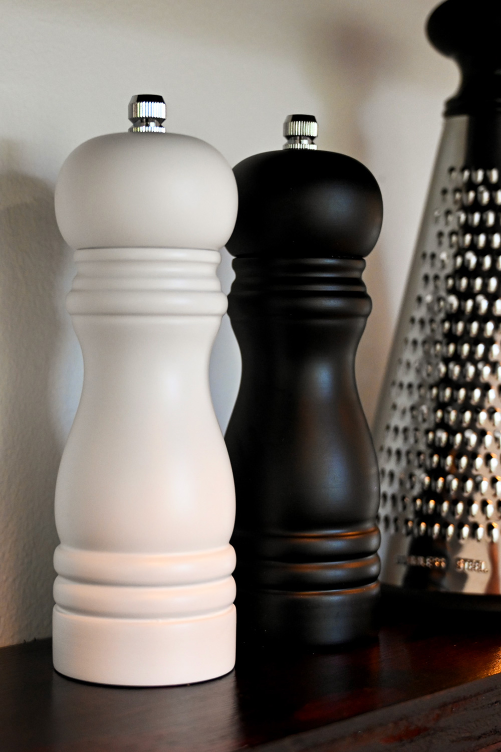 White and black salt and pepper mills on a wooden kitchen shelf