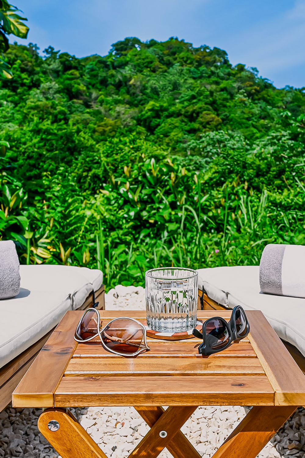 Outdoor lounge chairs and wooden table with sunglasses overlooking lush tropical mountains