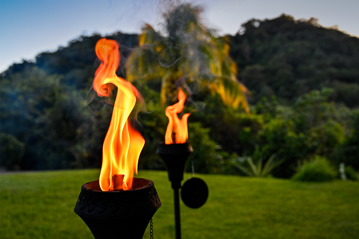 Torch flame glowing at dusk beside the mountain ridge during a private campfire experience at Hacienda Eterna Primavera in Puerto Rico.