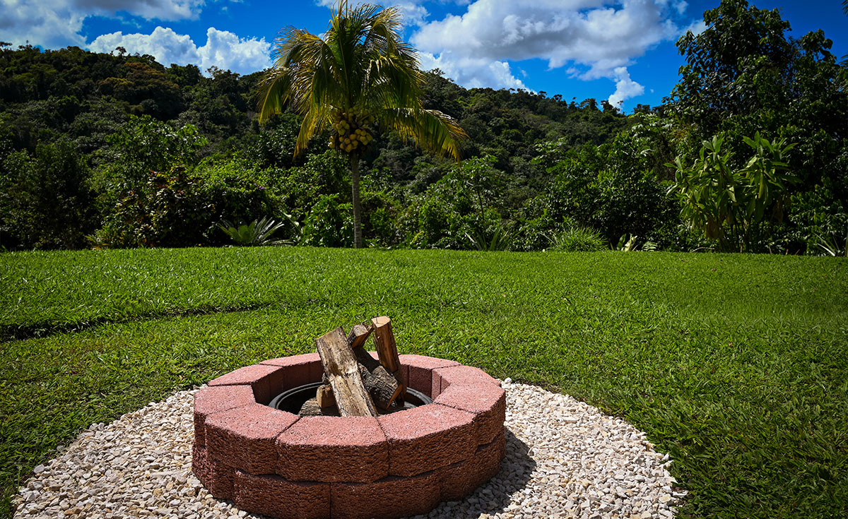 Private campfire pit setup at Hacienda Eterna Primavera in the mountains of Puerto Rico, surrounded by tropical greenery and open lawn.